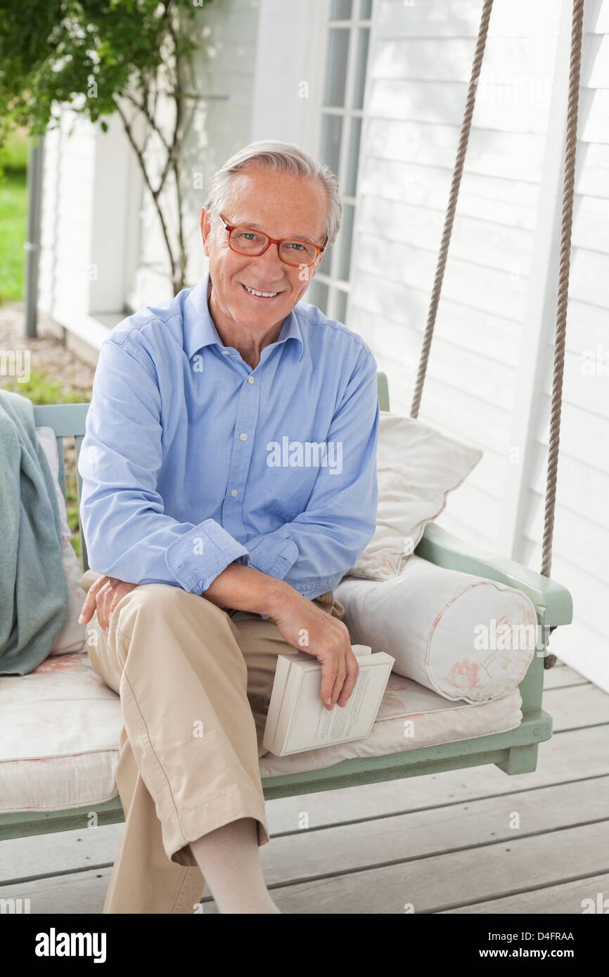 Uomo sorridente seduta sul portico swing Foto Stock