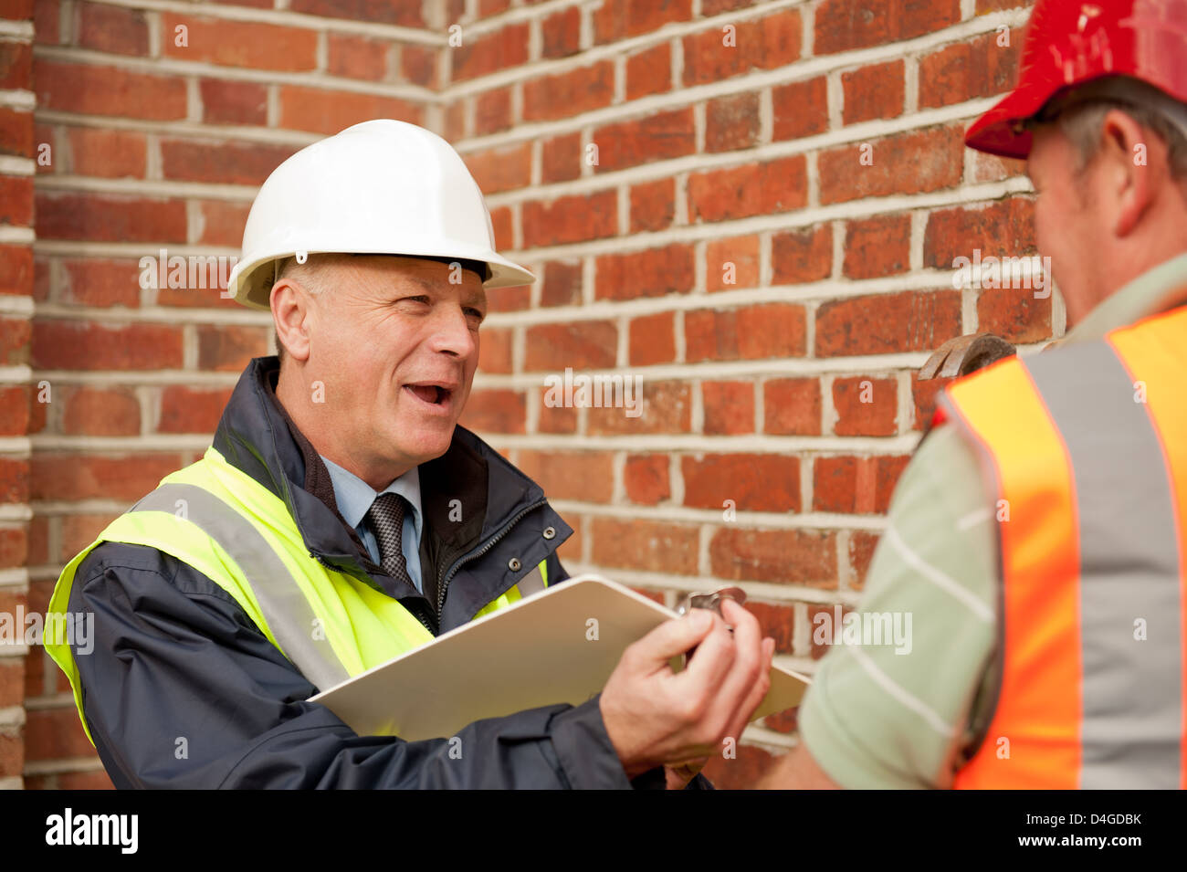 Builder facendo lavori di riparazione ad un muro di mattoni con la costruzione di ispettore di parlare e prendere appunti. Foto Stock