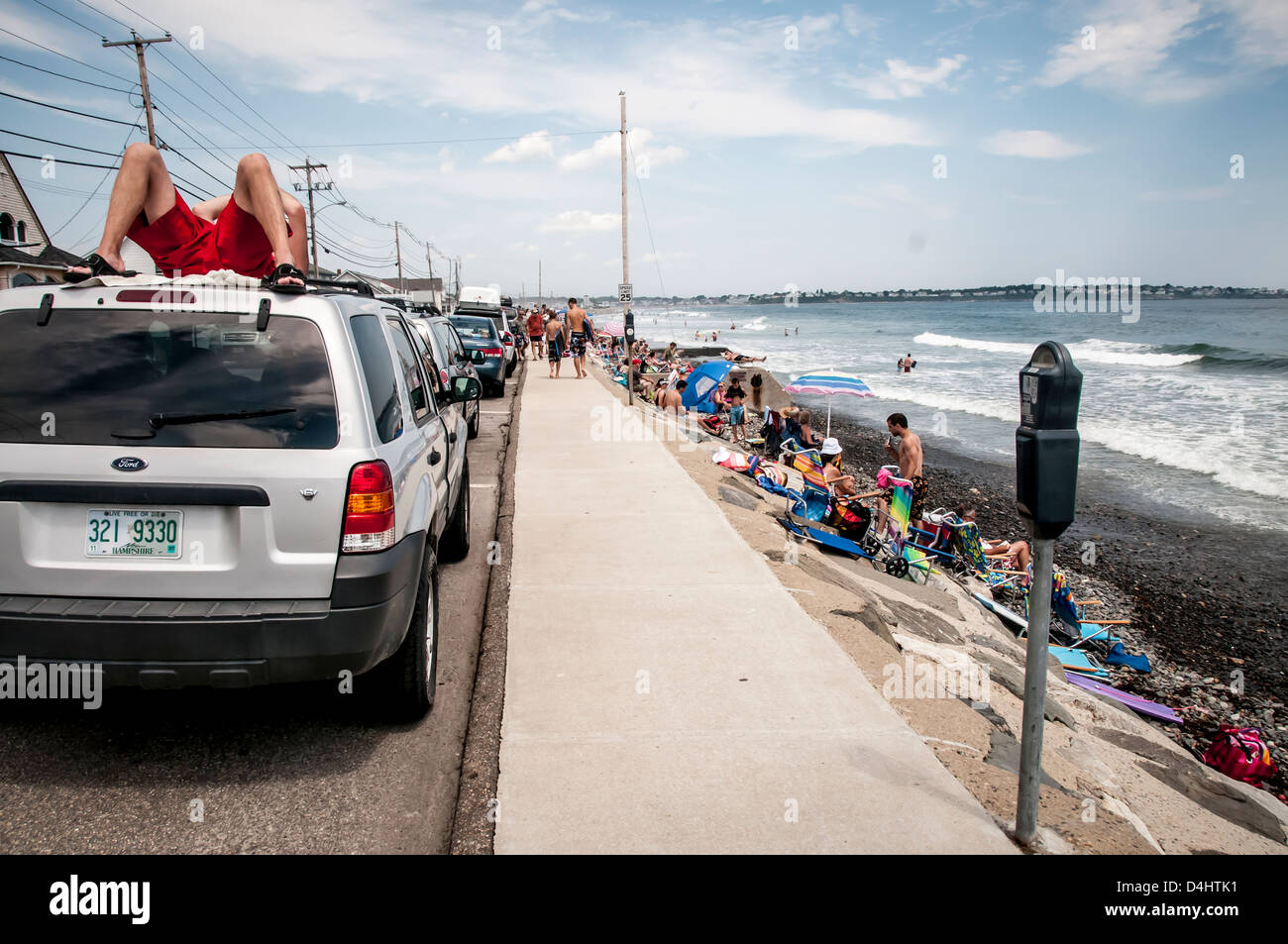 Ingegno, a questo affollato spiaggia di alta marea, e non vi è alcuna camera, questo giovane uomo mette il suo asciugamano sul tetto della sua vettura. Foto Stock