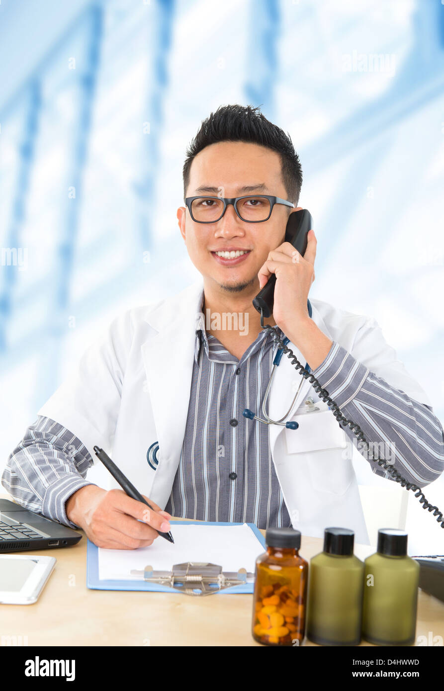 Giovani del Sud Est Asiatico medico a scrivere una nota durante la chiamata sul telefono cellulare Foto Stock
