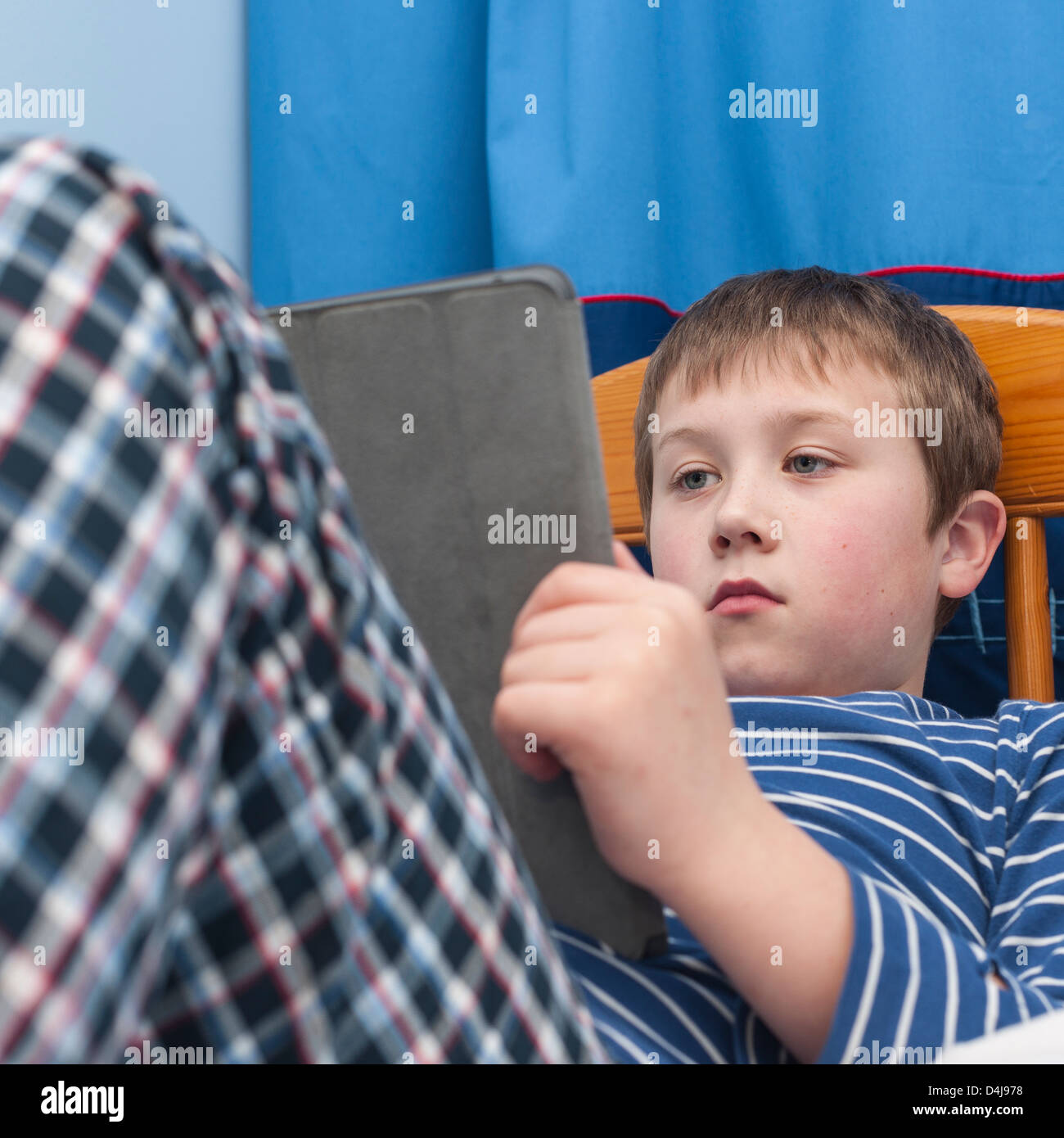 Un bambino di nove anni utilizzando il suo tablet ipad nella sua camera da letto Foto Stock