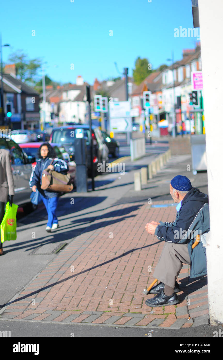 Un musulmano uomo seduto su un passo su una strada per lo shopping in Bury Park, Luton. Foto Stock
