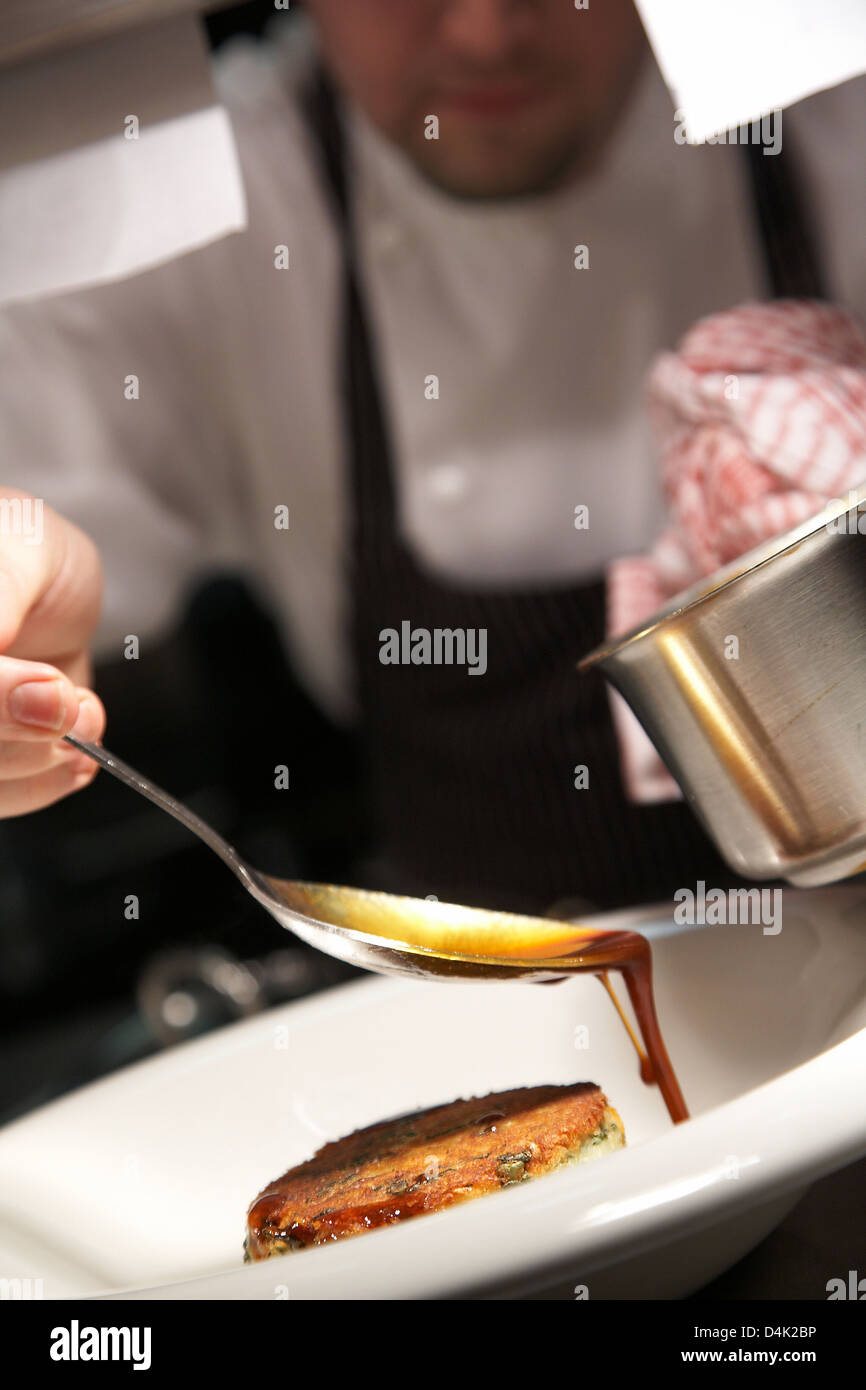 Lo Chef drizzling gravy sopra una patata e il segnale di PEA Röstinchen in ristorante nel Regno Unito. Foto Stock