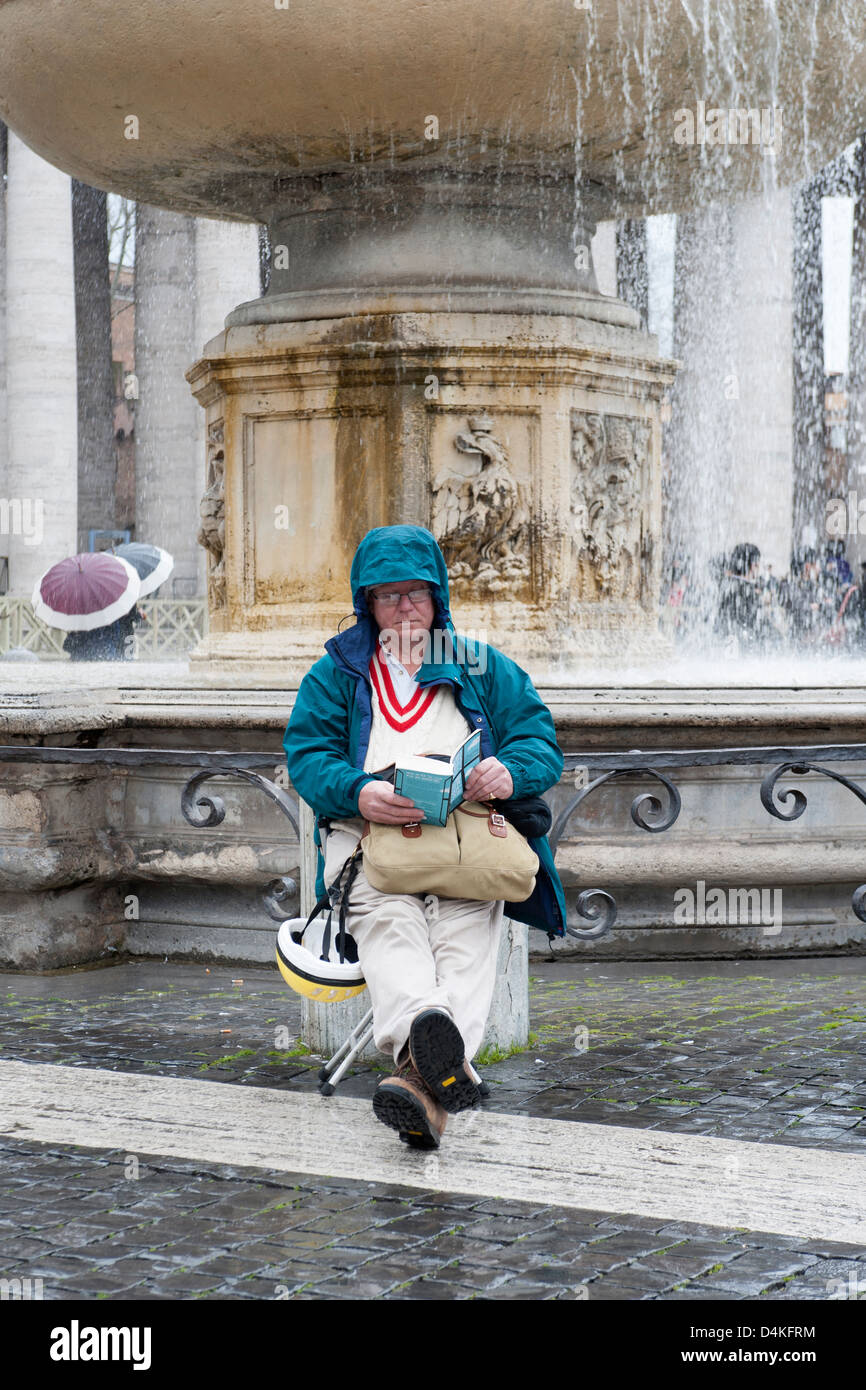 Uomo con impermeabile o leggere un libro in piazza San Pietro. Foto Stock