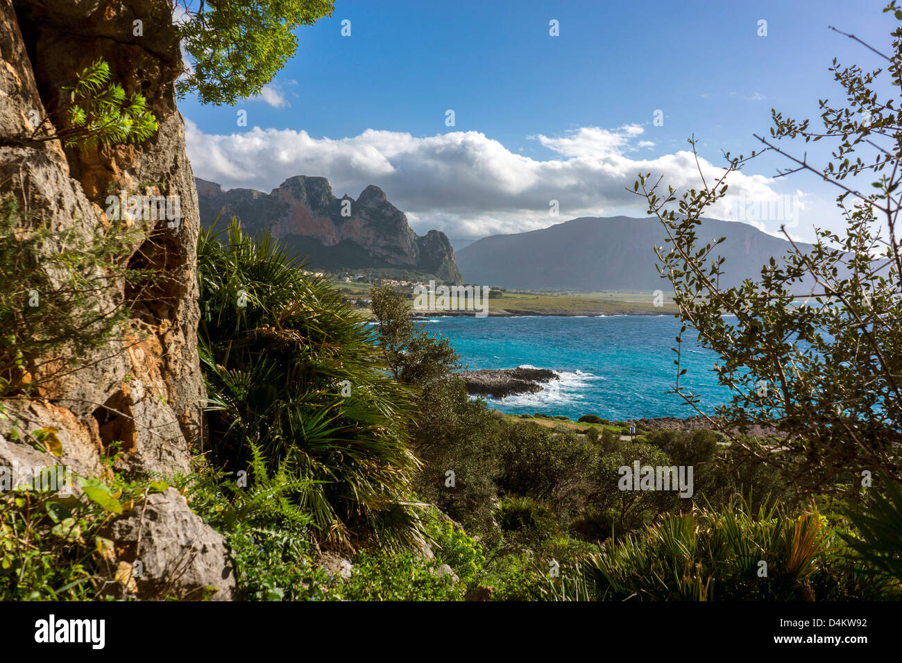 La molla verde paesaggio roccioso blu del mare e montagne distanti, cumulus nuvole, San Vito lo Capo, Sicilia Foto Stock