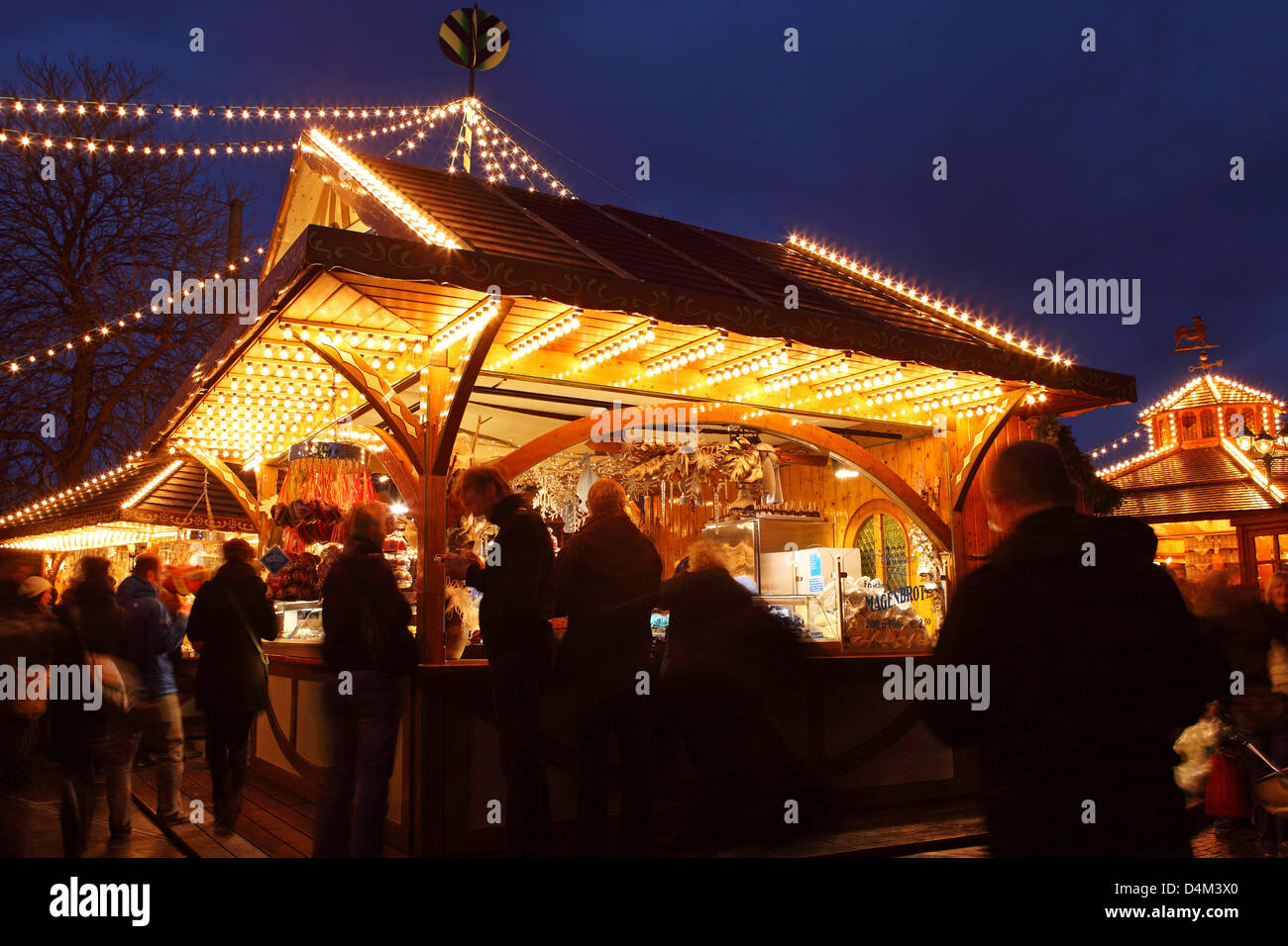 Le persone si incontrano attorno ad un illuminato in stallo il Mercato di Natale (Weihnachtsmarkt) a Stoccarda in Germania. Foto Stock