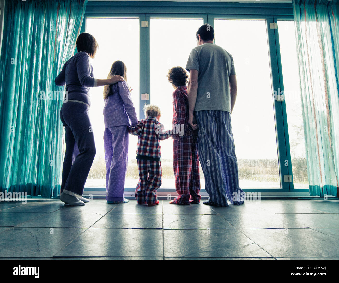 Famiglia in pigiama a guardare fuori dalla finestra Foto Stock