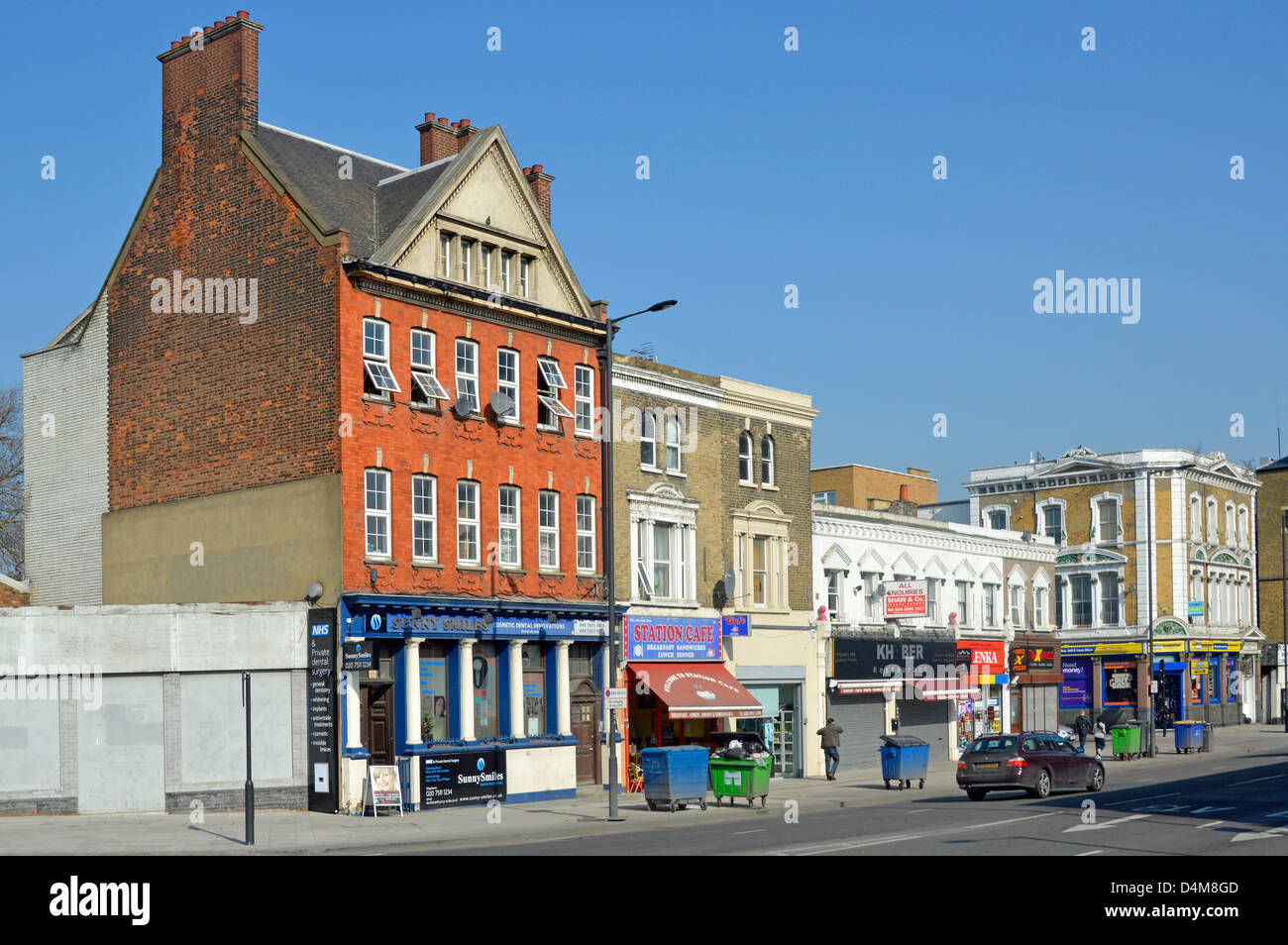 La Canning Town di vecchi edifici nella principale strada dello shopping con cestini della spazzatura fuori dei negozi in attesa di svuotamento Foto Stock