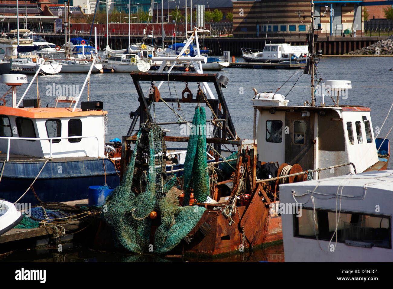 Piccola vecchia barca da pesca con rete e paranchi di sollevamento ormeggiata in porto turistico moderno con yachts in background Foto Stock