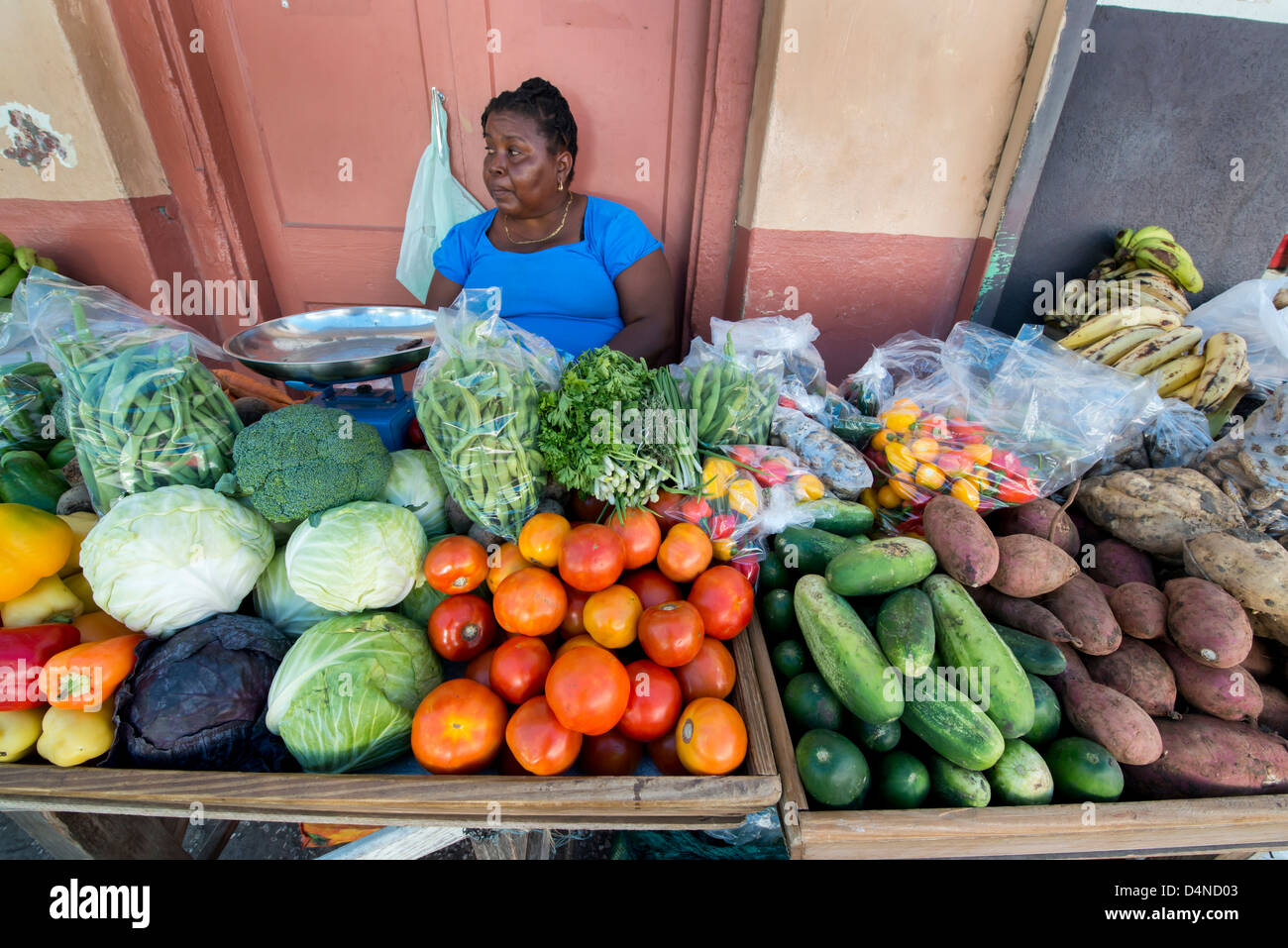 Una donna colorato la vendita di frutta e verdura su un mercato in stallo la strada in Speightstown, Barbados, Caraibi Foto Stock