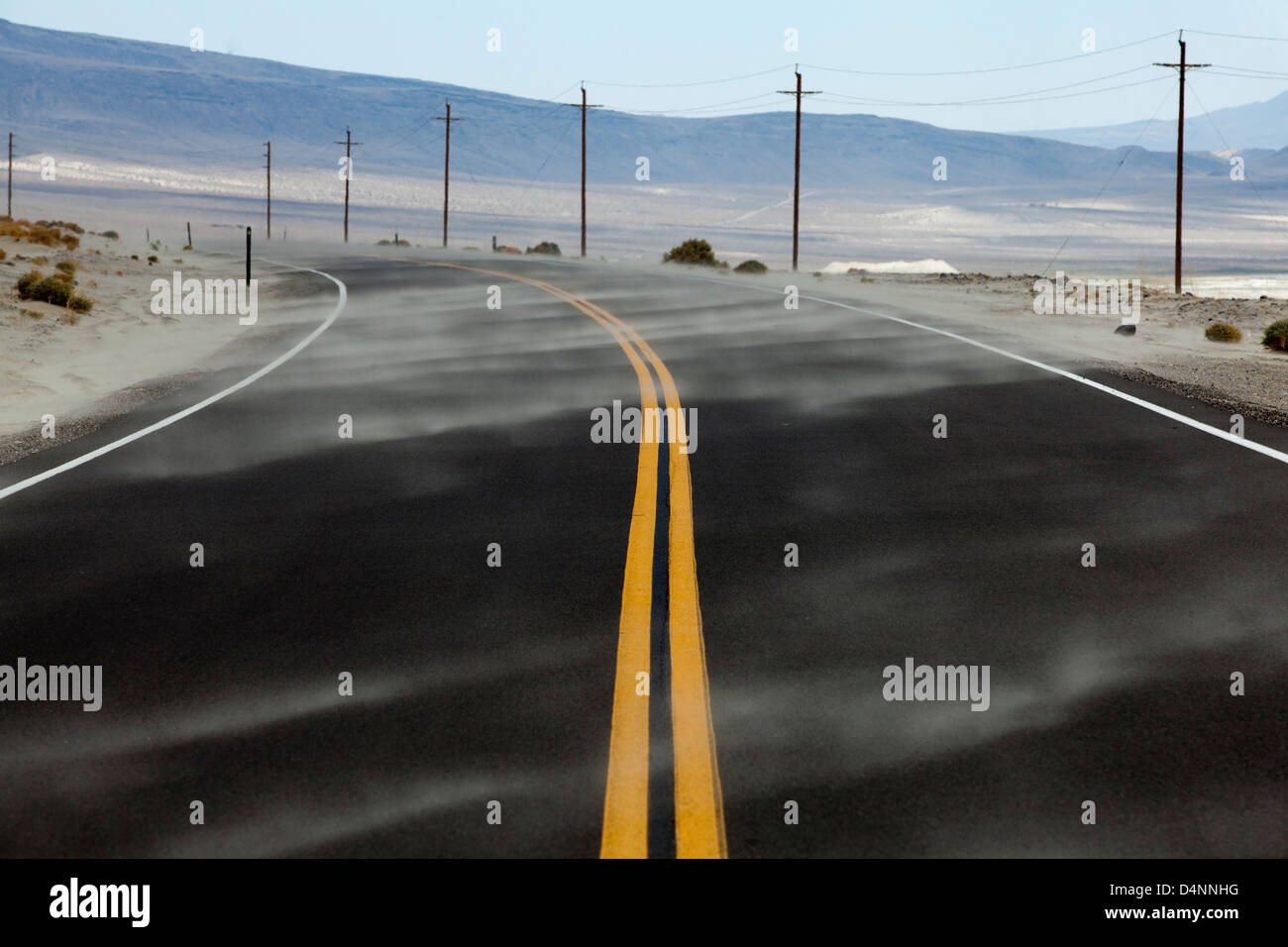 Soffiatura di sabbia attraverso la strada nella Valle della Morte del deserto, California, USA. Foto Stock