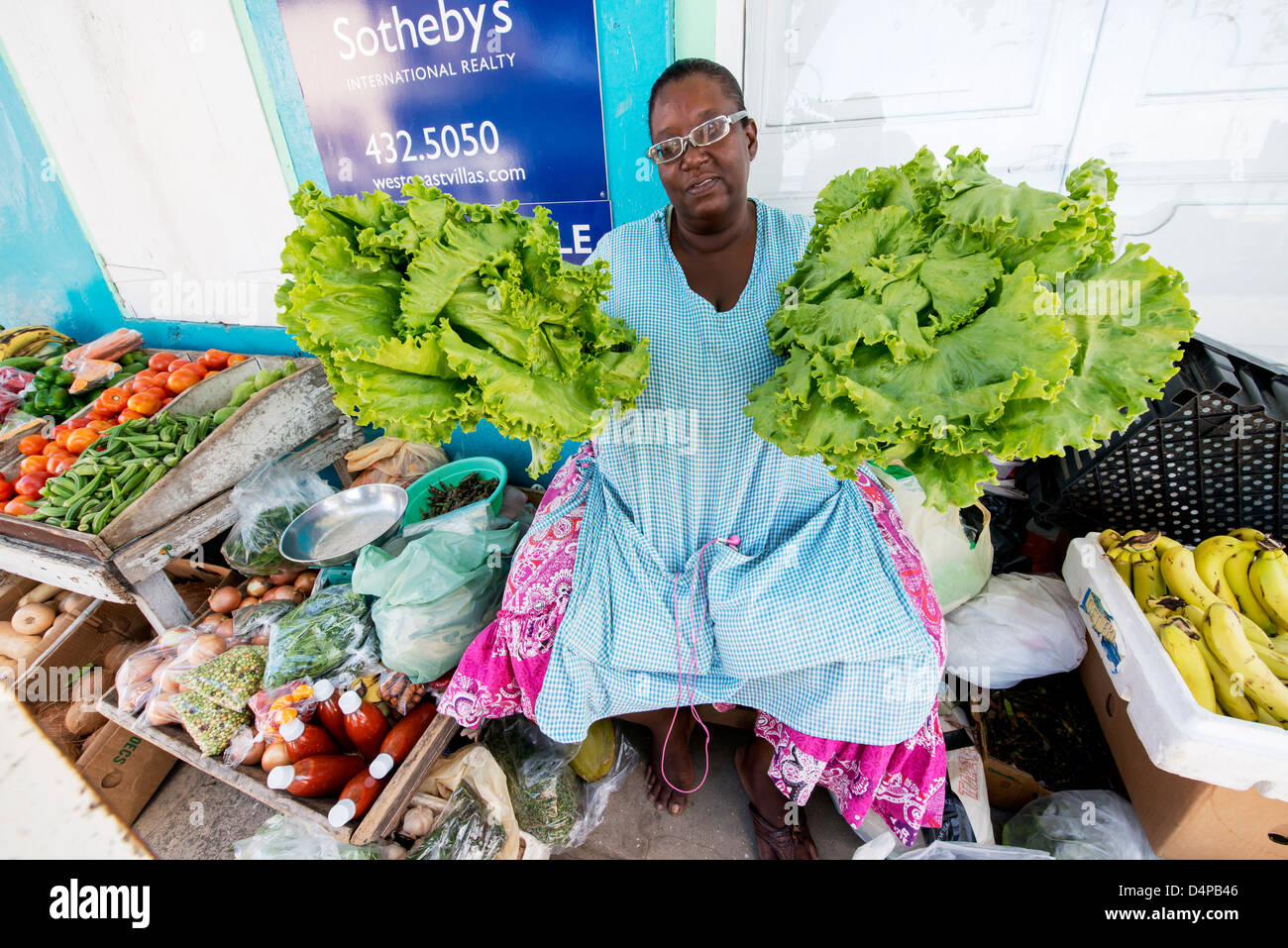 Una donna colorato la vendita di frutta e verdura su un mercato in stallo la strada in Speightstown, Barbados, Caraibi Foto Stock