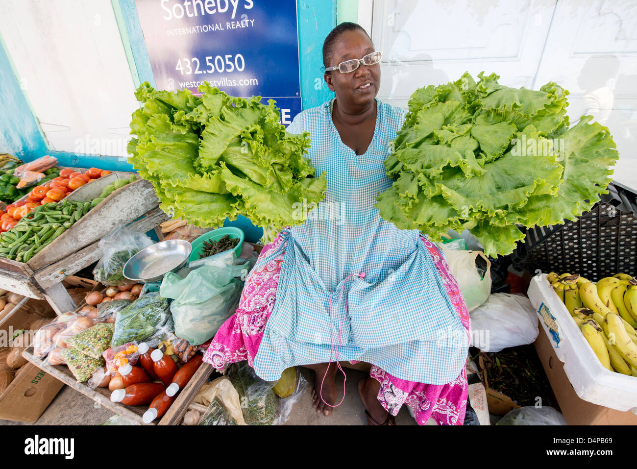 Una donna colorato la vendita di frutta e verdura su un mercato in stallo la strada in Speightstown, Barbados, Caraibi Foto Stock