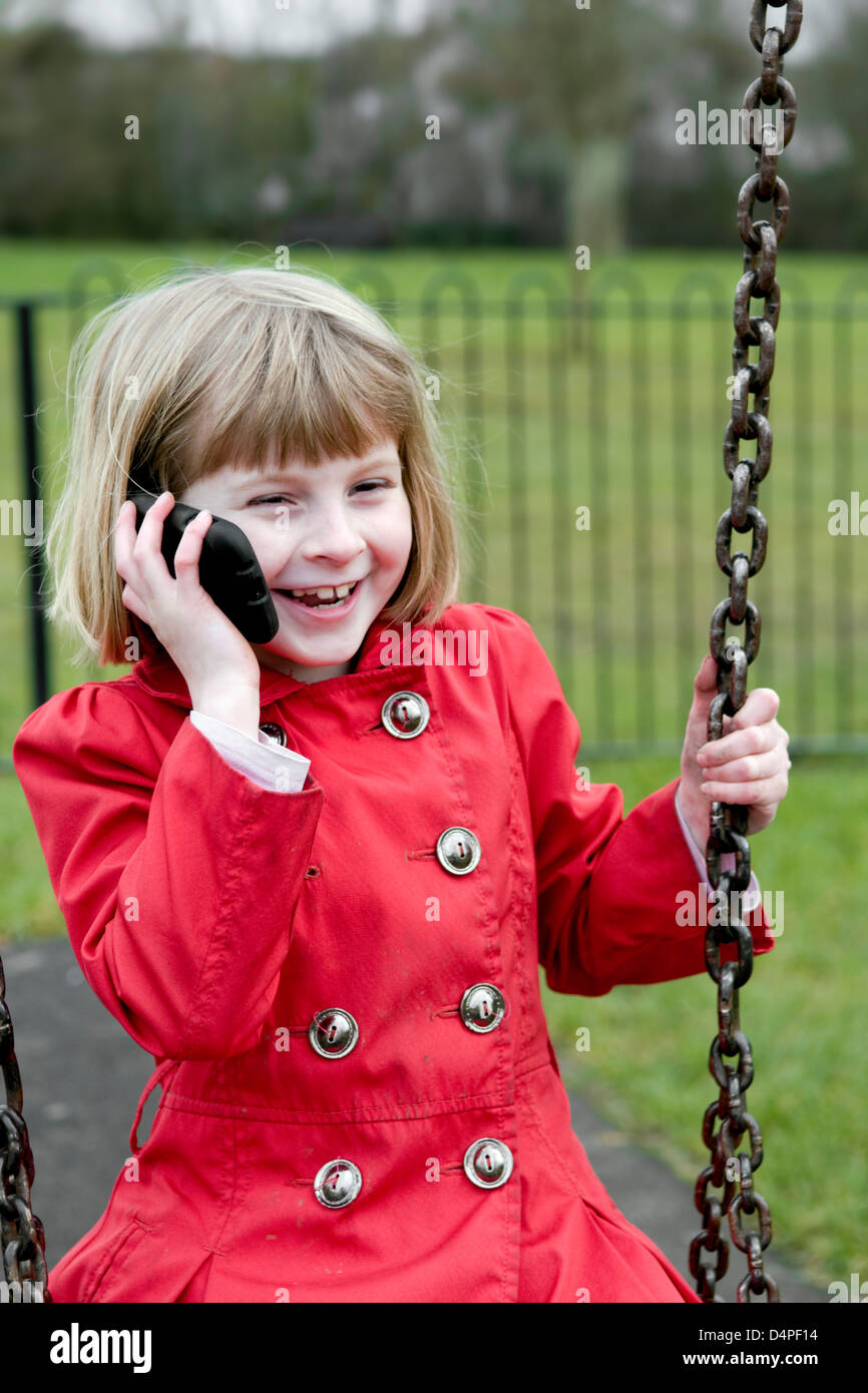 8 anno vecchia ragazza caucasica ridendo e parlando al telefono cellulare mentre dire sull'altalena. Foto Stock