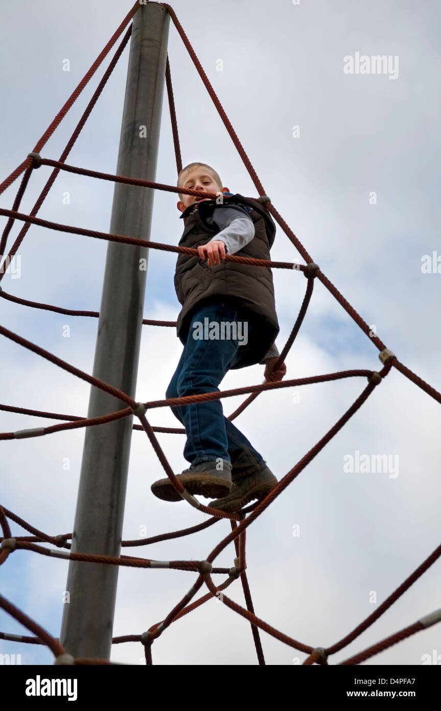 I giovani di 10 anni ragazzo caucasico arrampicata su una corda di telaio di arrampicata nel parco in Bristol, Regno Unito Foto Stock