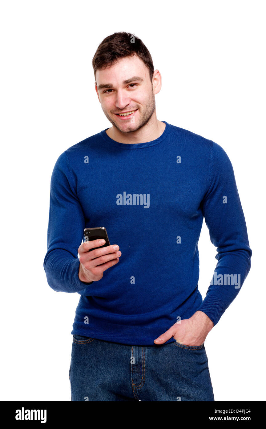 Attraente giovane uomo che indossa un maglione blu e jeans stava tenendo un telefono cellulare isolato su uno sfondo bianco Foto Stock