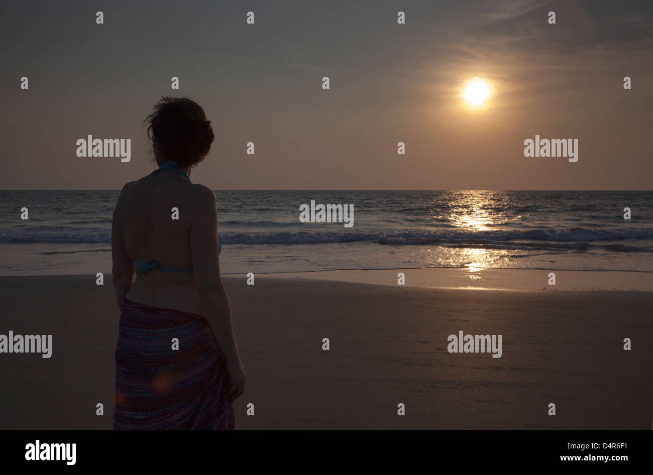 Una donna si affaccia al mare come il sole tramonta nel pomeriggio. Impostare su Arossim Beach, a sud di Goa, India. Foto Stock