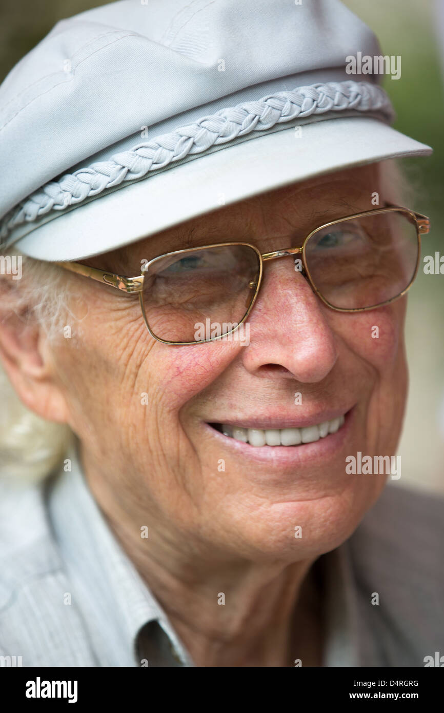 Senior uomo sorridente in telecamera con il suo cappello e occhiali. Foto Stock