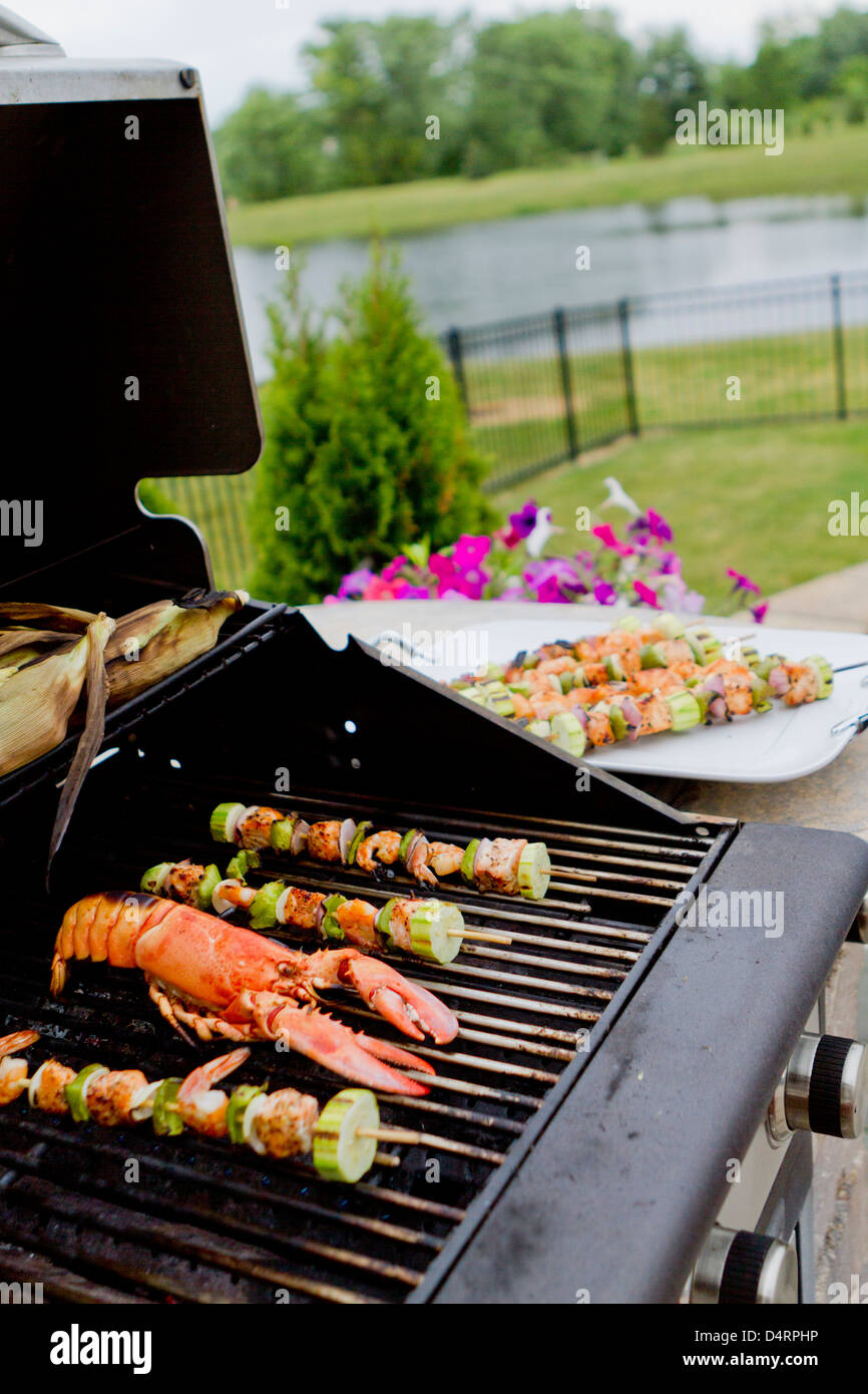 Pesce del Mediterraneo shish kebab e aragosta su il barbecue è quasi pronto. Persone che soffrono la fame in attesa. Foto Stock