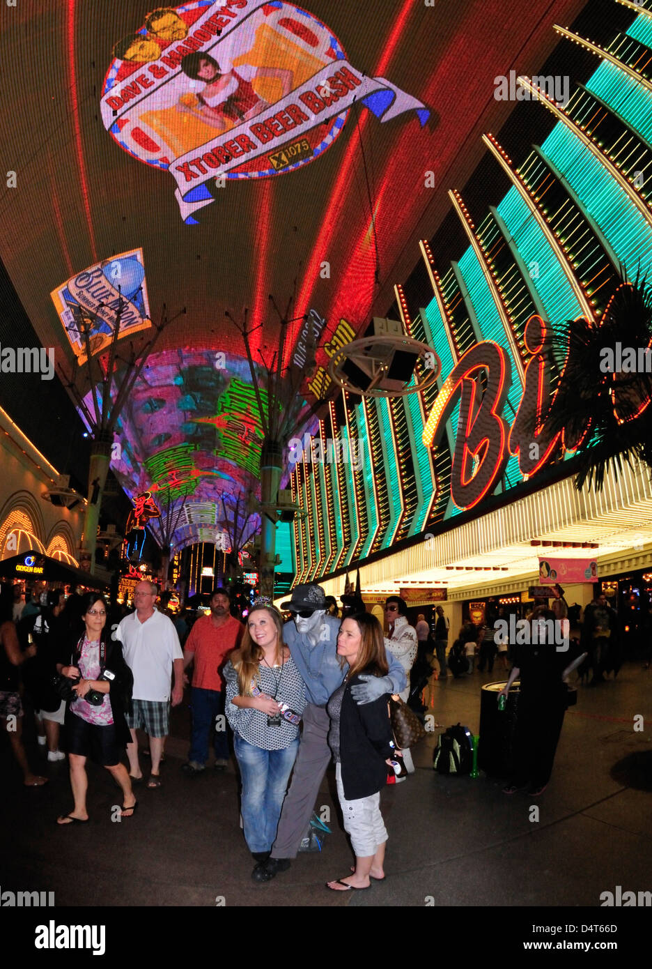 Circondato da luci al neon, una coppia di donne sono abbracciati su Fremont Street, Las Vegas, da un carattere spettrale con pelle color argento Foto Stock