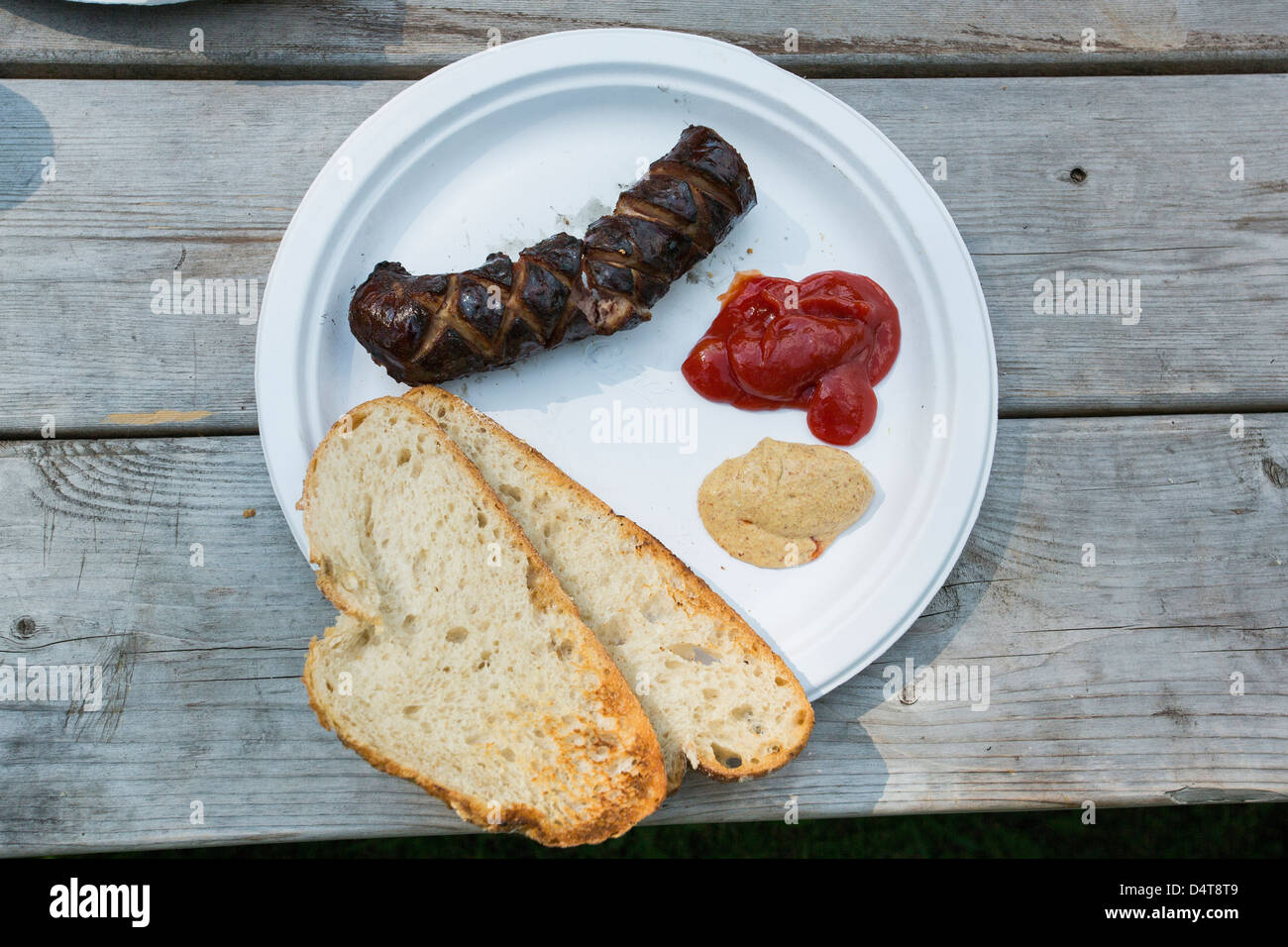 Grigliata di fresco/kielbasa salsiccia e pane con ketchup e senape su un foglio di carta bianca piastra, in legno Tavolo picnic Foto Stock