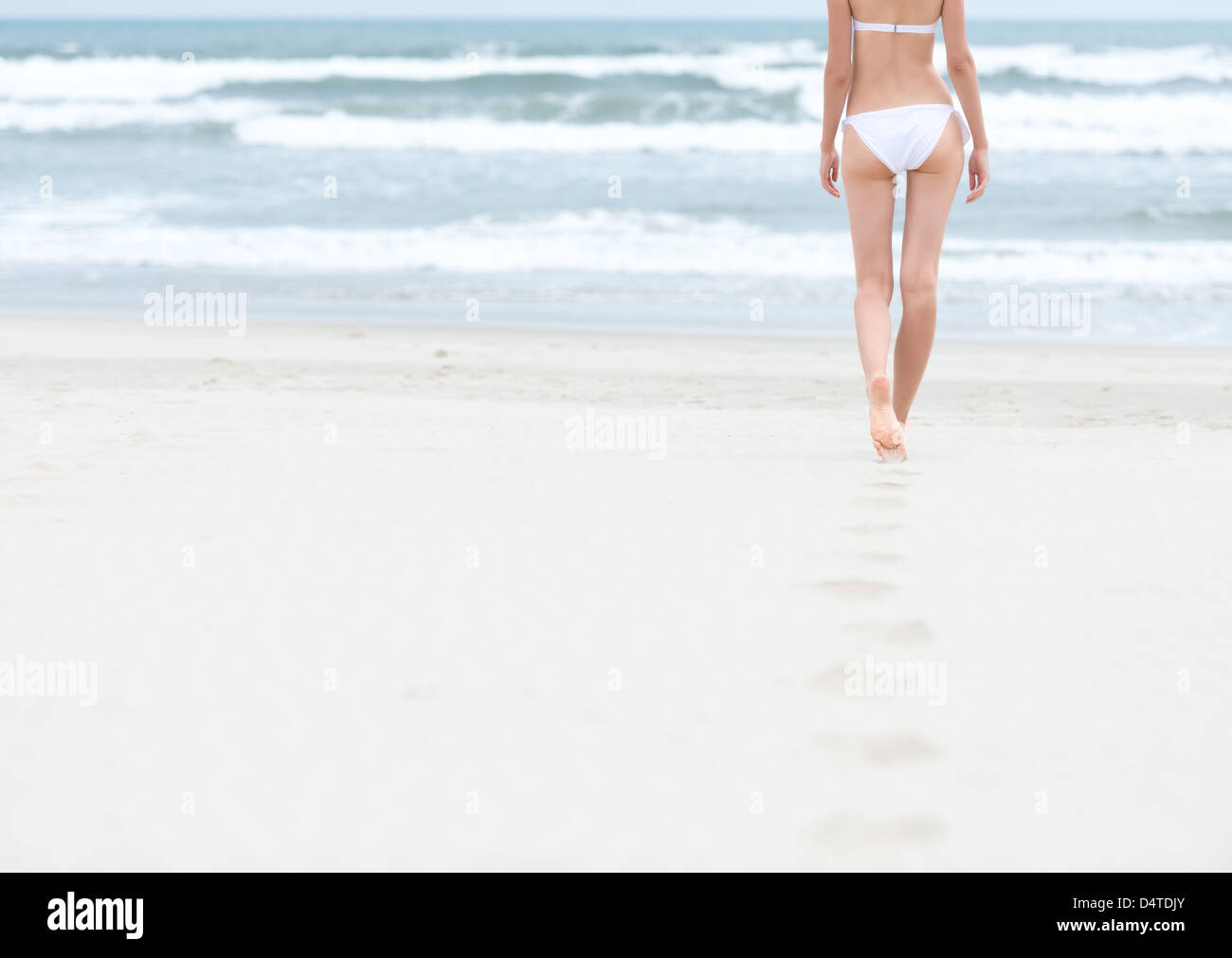 Slim giovane donna in costume da bagno bianco a piedi al mare o oceano di  lasciare impronte sulla sabbia morbida. Blu oceano onde con schiuma in  backgr Foto stock - Alamy