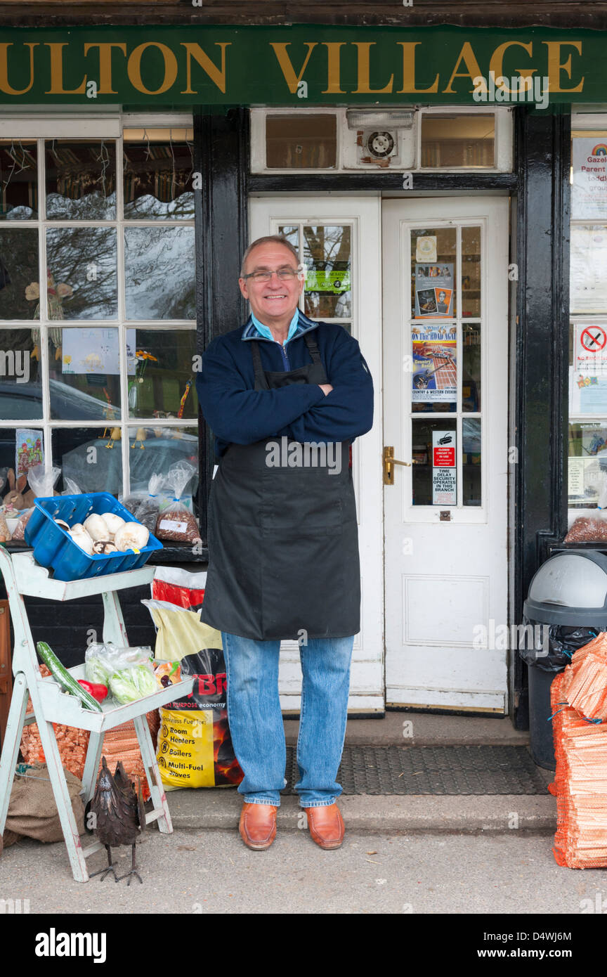 La Moulton village memorizza un tradizionali magazzini generali e ufficio postale in Suffolk REGNO UNITO con il negoziante in piedi al di fuori. Foto Stock