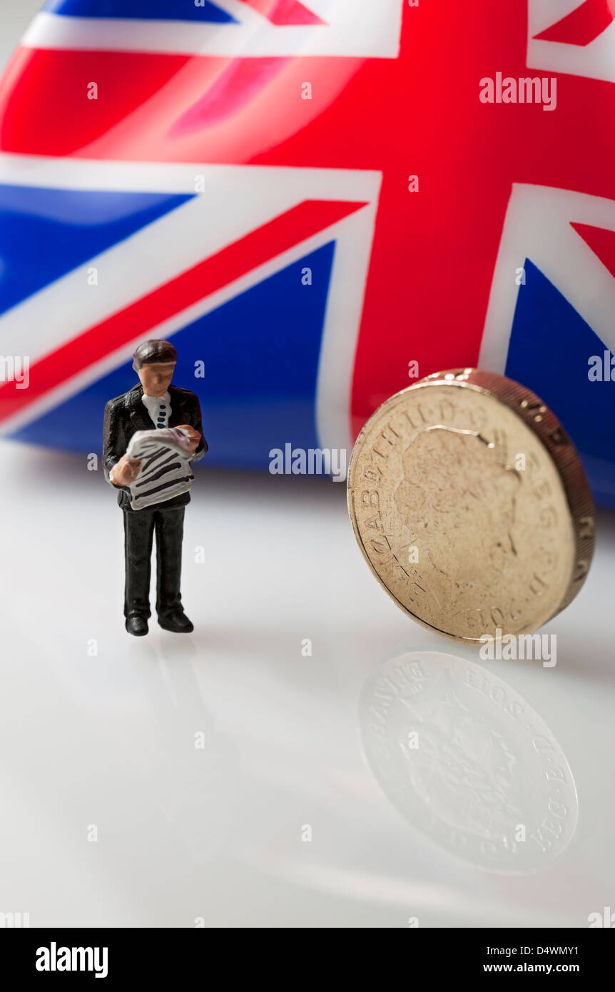 Primo piano di Toy, piccola figura di un uomo d'affari, uomo di sesso maschile, si trovava accanto a un concetto di business finance di moneta inglese Sterling Foto Stock