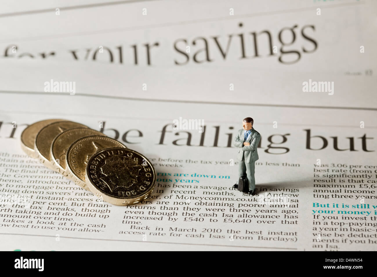 Primo piano di un giocattolo piccola figura di un uomo maschio si trovava accanto alle monete inglesi sulla pagina del concetto di finanza aziendale dei giornali finanziari Foto Stock