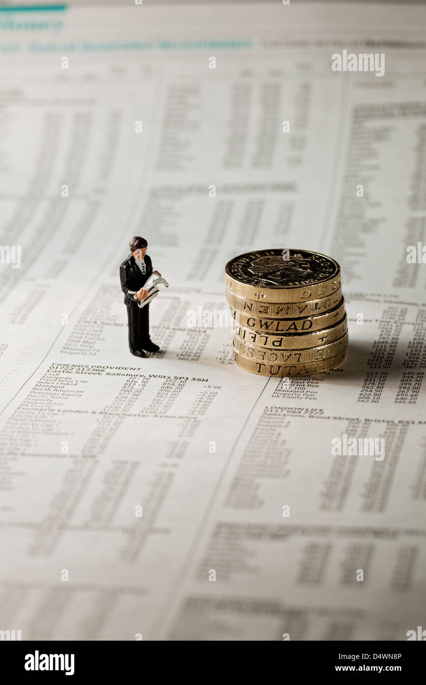 Primo piano di un giocattolo, la piccola figura di un uomo d'affari maschile si trovava accanto alle monete inglesi sulla pagina del concetto di finanza aziendale dei giornali finanziari Foto Stock