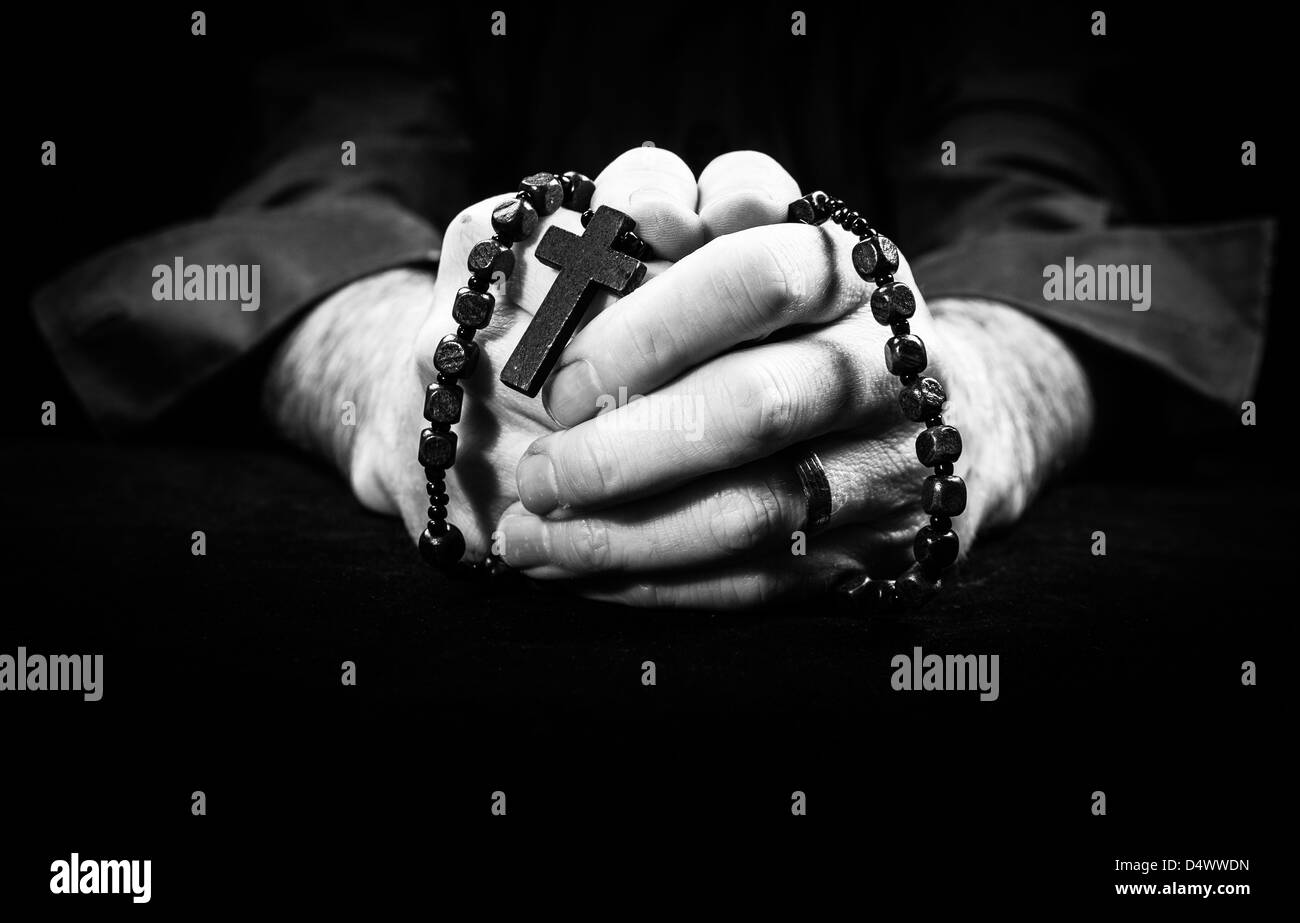 Mani tenendo i grani del rosario e croce pregando. Foto Stock