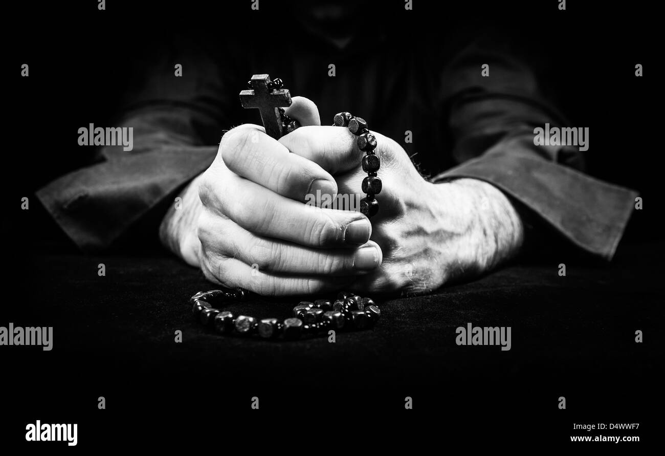 Mani tenendo i grani del rosario e croce pregando. Foto Stock