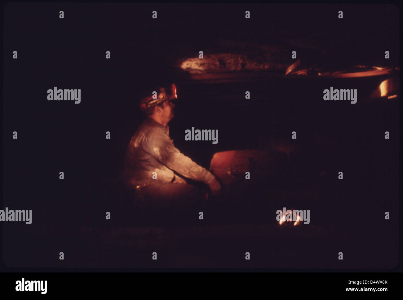 Questa fotografia del 1974 mostra un minatore in una miniera sotterranea illuminata dalla luce della lampada di un collega. L'immagine cattura anche un'auto con otturatore, utilizzata per il trasporto di personale addetto alla sicurezza e piccoli gruppi. Foto Stock