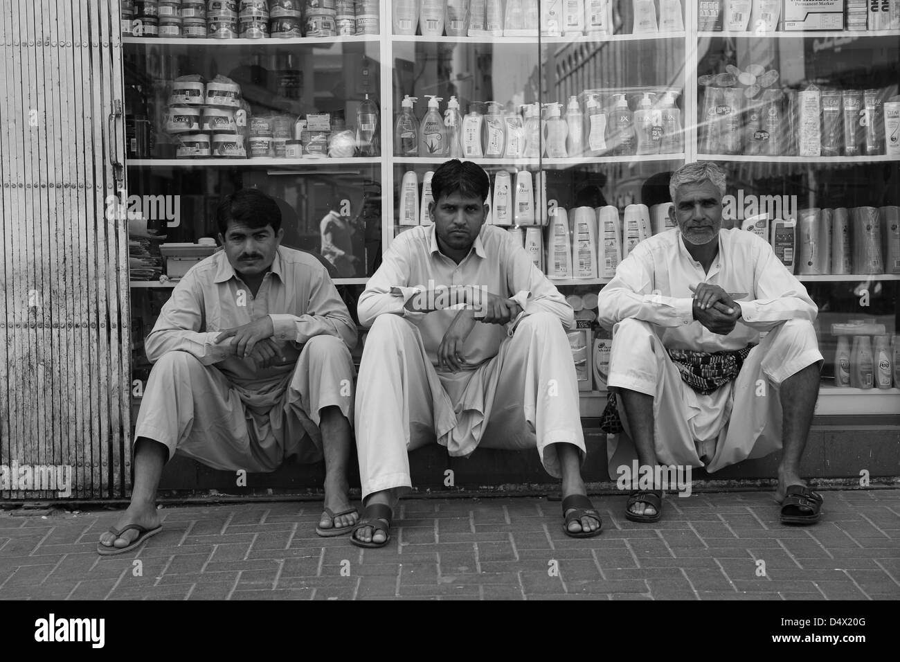 Tre uomini seduti nella parte anteriore del negozio finestra, Dubai, Emirati Arabi Uniti Foto Stock