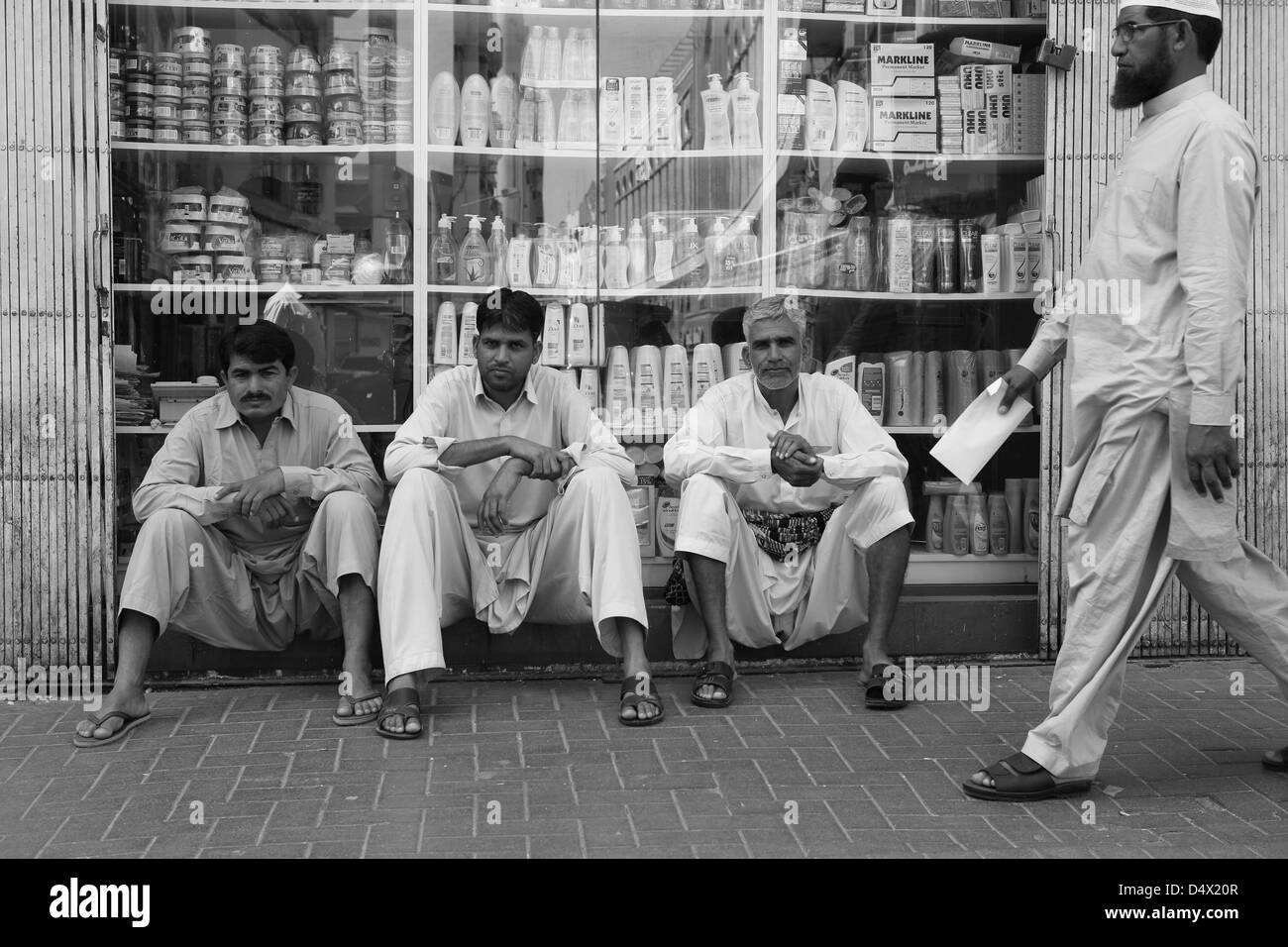 Tre uomini seduti nella parte anteriore del negozio finestra, Dubai, Emirati Arabi Uniti Foto Stock