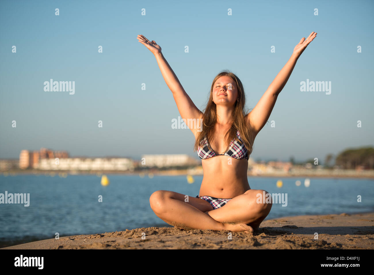 Giovane donna bionda rilassante fare yoga sulla spiaggia di sabbia di mare e yacht sullo sfondo Foto Stock