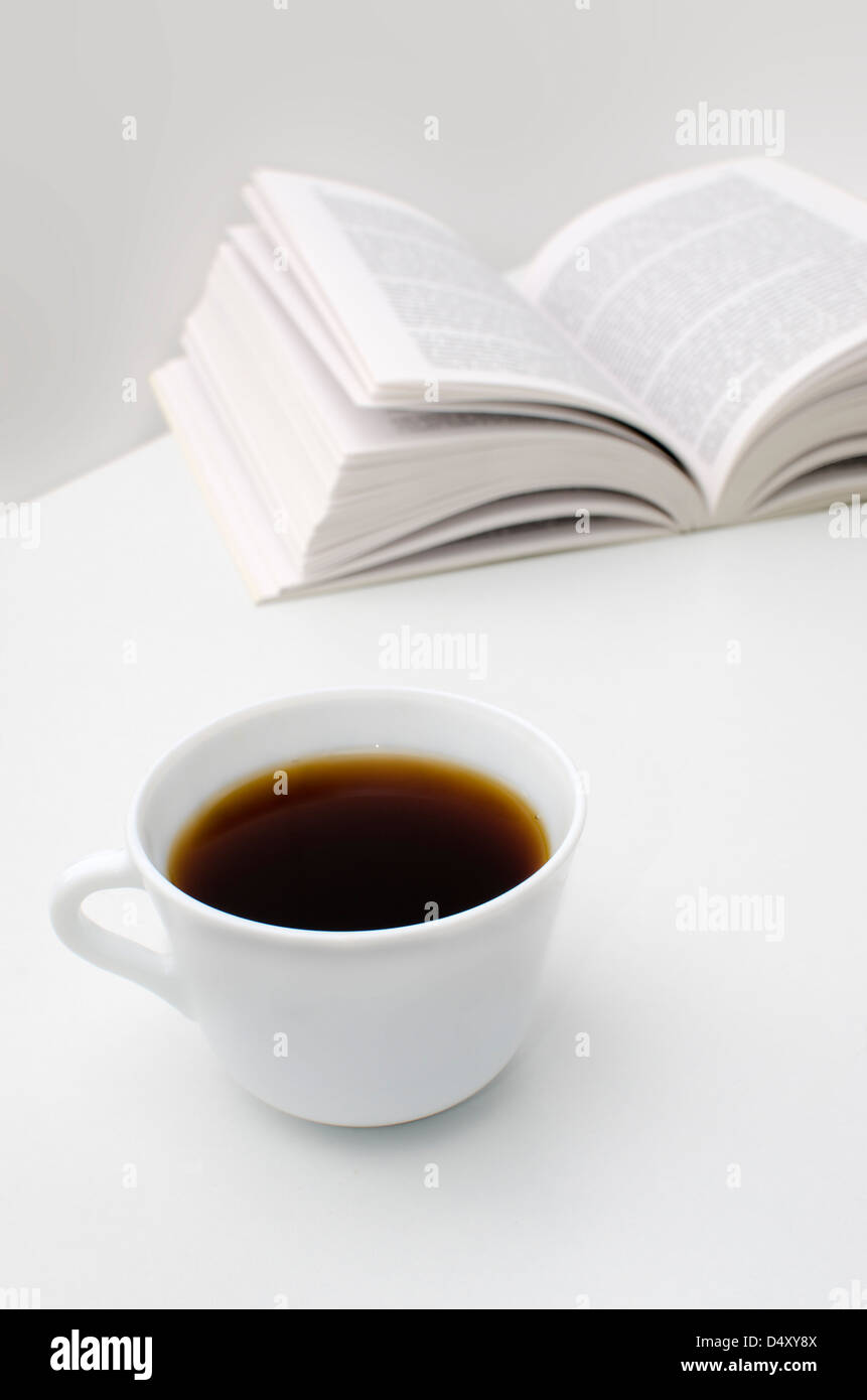 Messa a fuoco selettiva su una tazza di caffè, libro aperto sul fondo. elevato la chiave Foto Stock