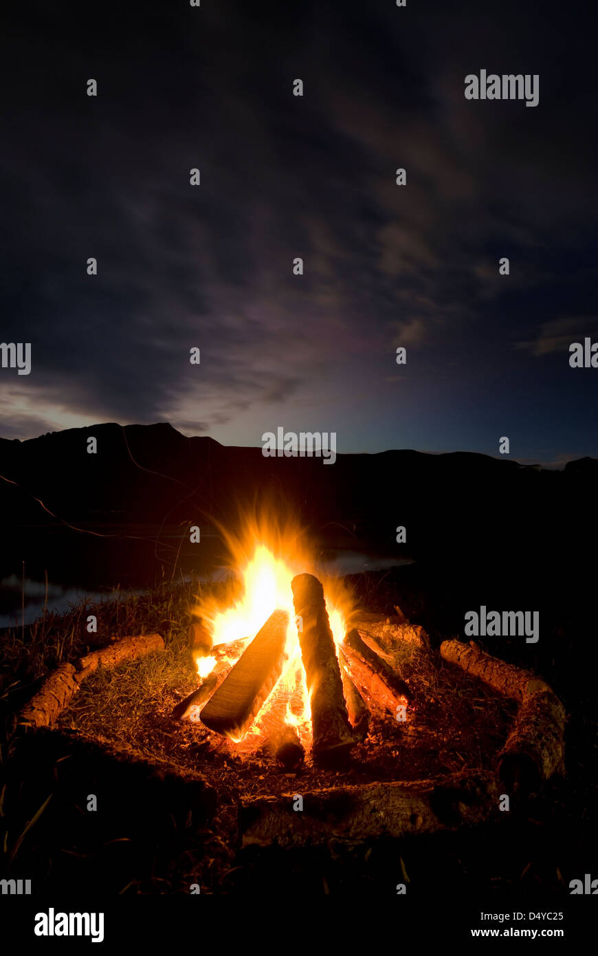 Fuoco di campo con i registri disposti intorno al fuoco accanto a lago e montagne, Nuova Zelanda Foto Stock