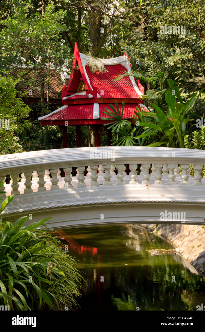 Thailandia, Bangkok. Il Museo Prasart. Serenità giardino, ponte sul laghetto in giardino con rosso edificio Thai. Foto Stock