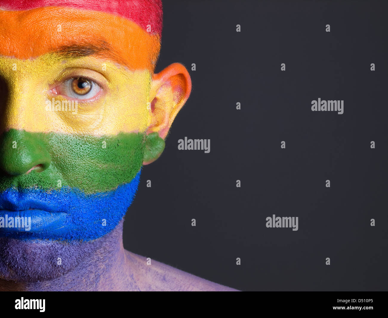 L'uomo con il suo volto dipinto con la bandiera multicolore gay Foto Stock