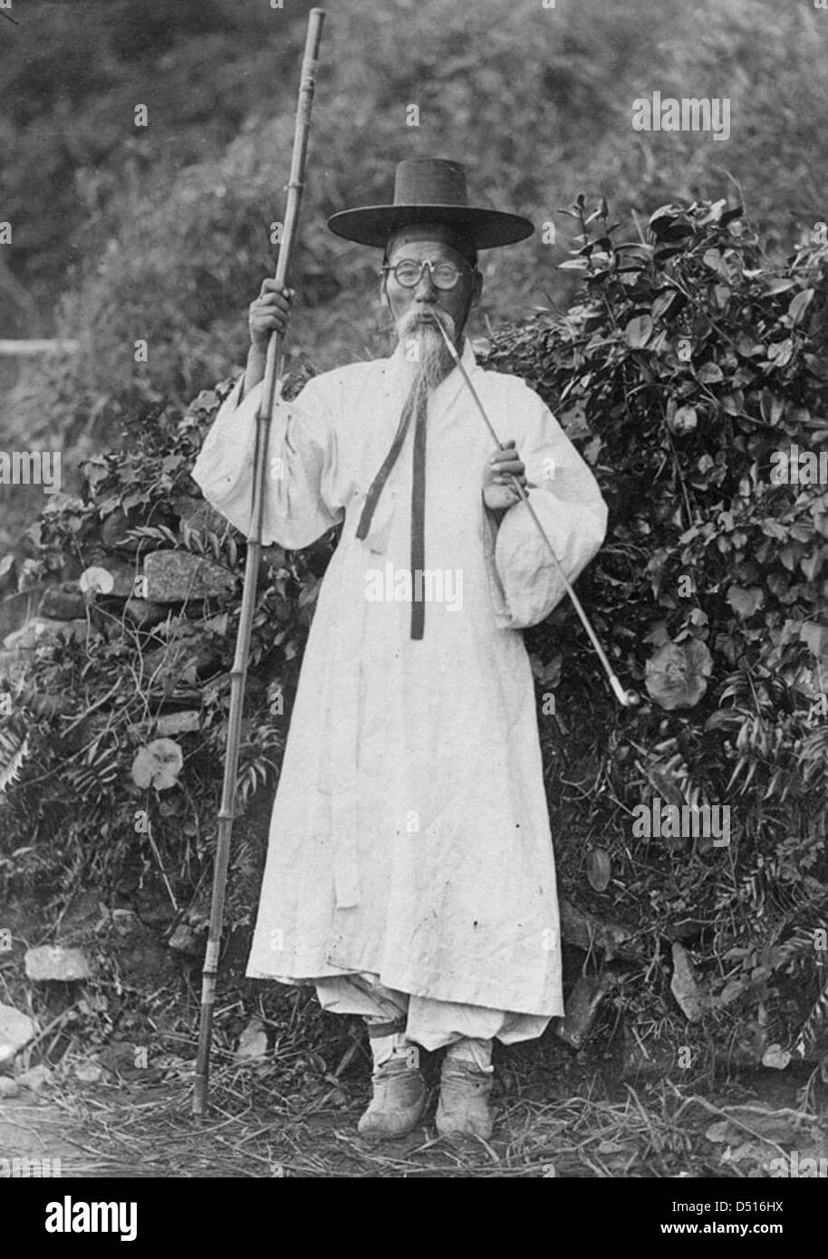 Una fotografia di un uomo coreano in abbigliamento tradizionale, con un crine di cavallo e un cappello di bambù, tipico degli anni '1880 L'uomo è in piedi all'aperto, indossando stivali e occhiali da vista, mostrando la storica moda coreana. Foto Stock