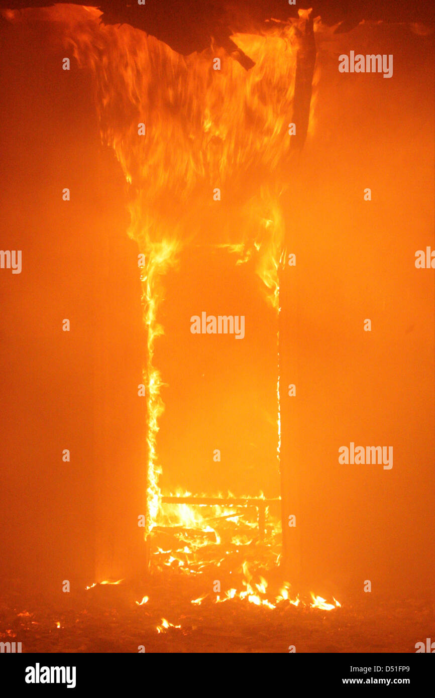 Il vecchio edificio in pieno inferno di fiamme e un vigile del fuoco combattere le fiamme Foto Stock