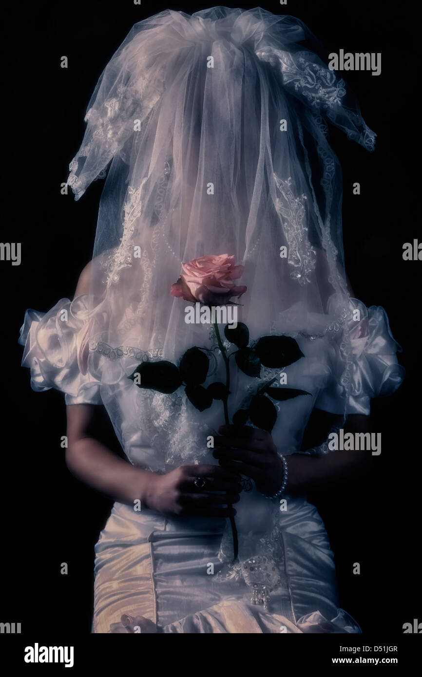 Una sposa con una rosa rosa e un velo di fronte il suo volto Foto Stock