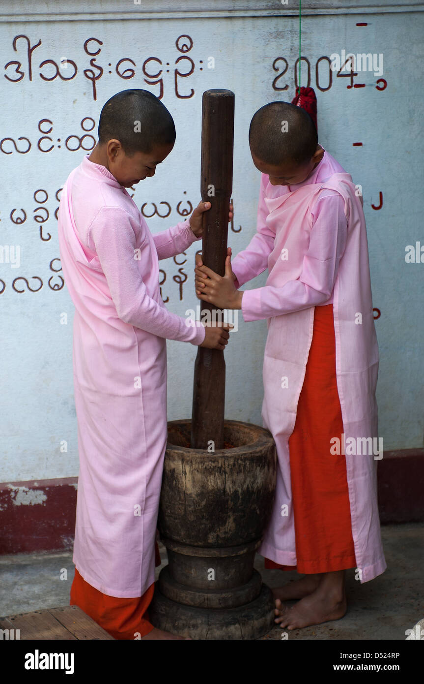 Due giovani suore in un convento vicino a Mandalay utilizzare un gigante pestello per macinare pasta di peperoncino per la comunità di pranzo. Foto Stock