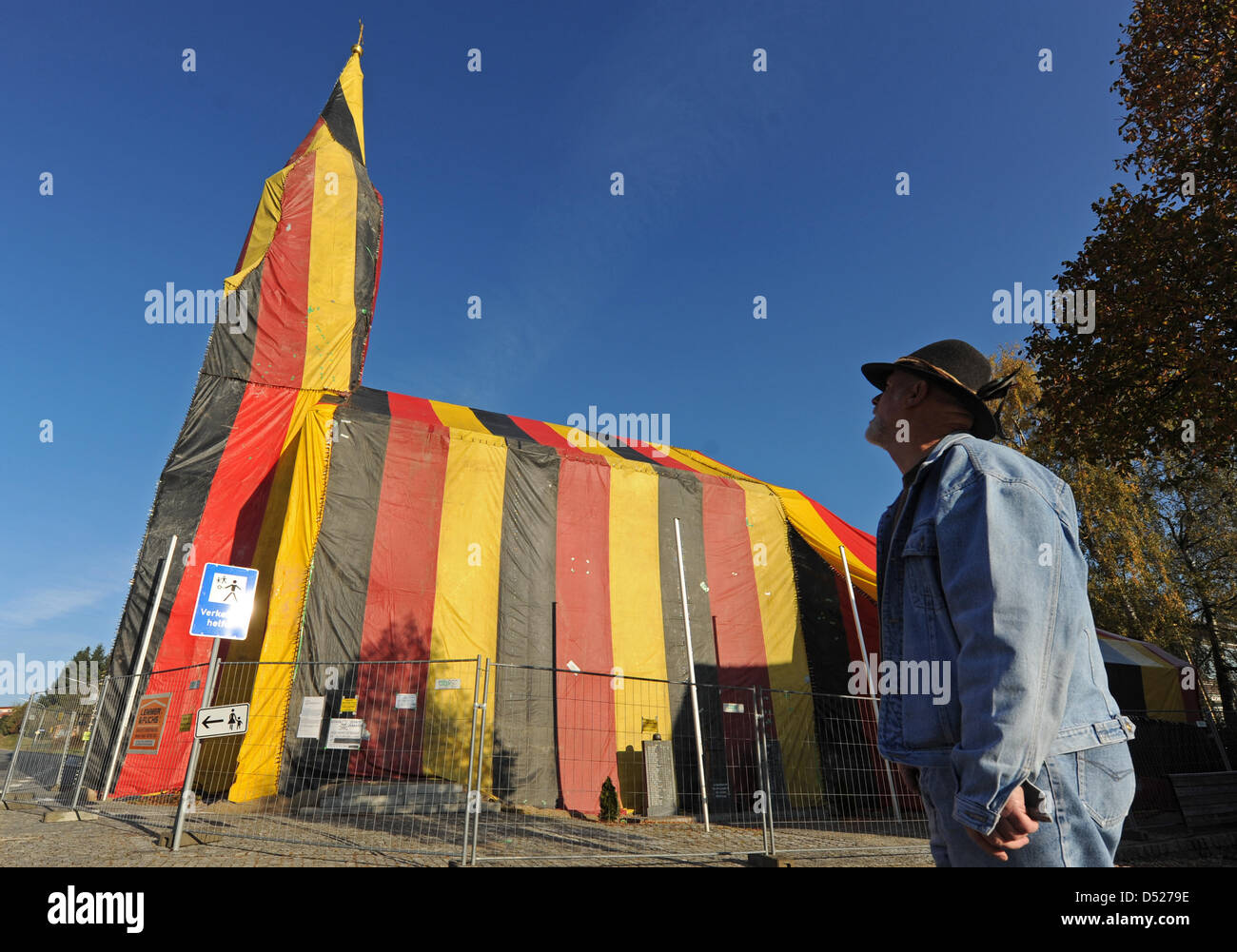 Ein Mann steht am Freitag (22.10.2010) in Zinzenzell (Niederbayern) vor einer verhüllten Kirche. Eine Firma für Materialschutz hat die Sankt-Michaels-Kirche komplett in eine Folie mit den Nationalfarben eingepackt. Um den Holzwurm im Holz des Gotteshause zu beseitigen, ist das Gebäude begast worden. Foto: Armin Weigel dpa/lby Foto Stock