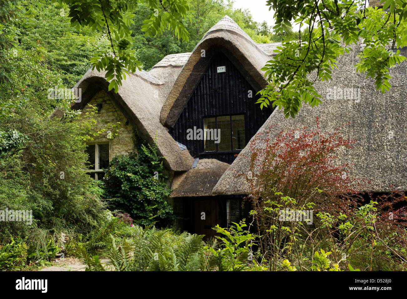 Un idilliaco arti e mestieri in stile cottage con il tetto di paglia circondate da boschi, Gloucestershire, England, Regno Unito Foto Stock
