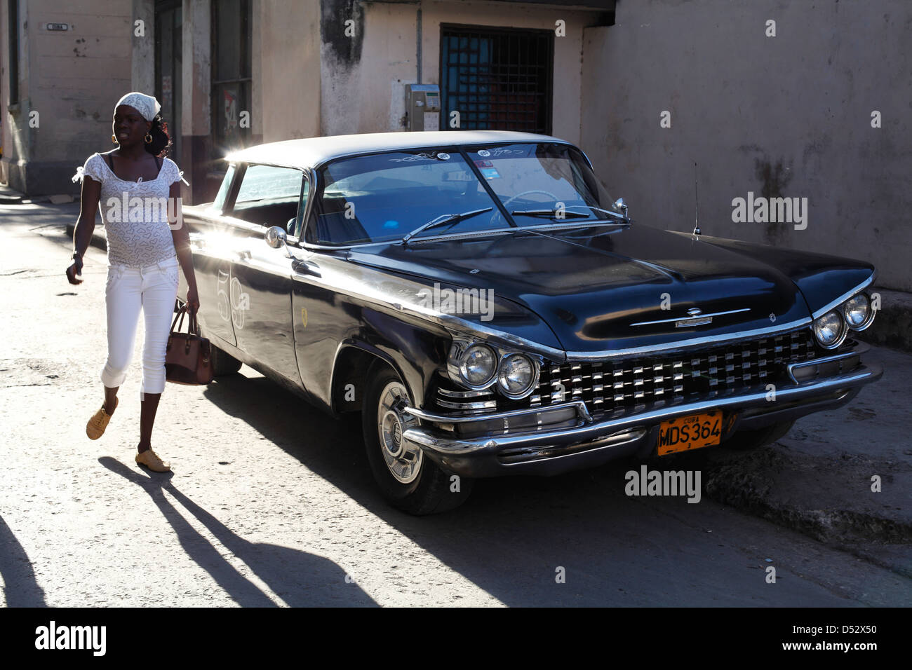 Bella giovane donna camminare davanti a un classico vecchio Buick Electra 220 sulle strade di La Habana Foto Stock
