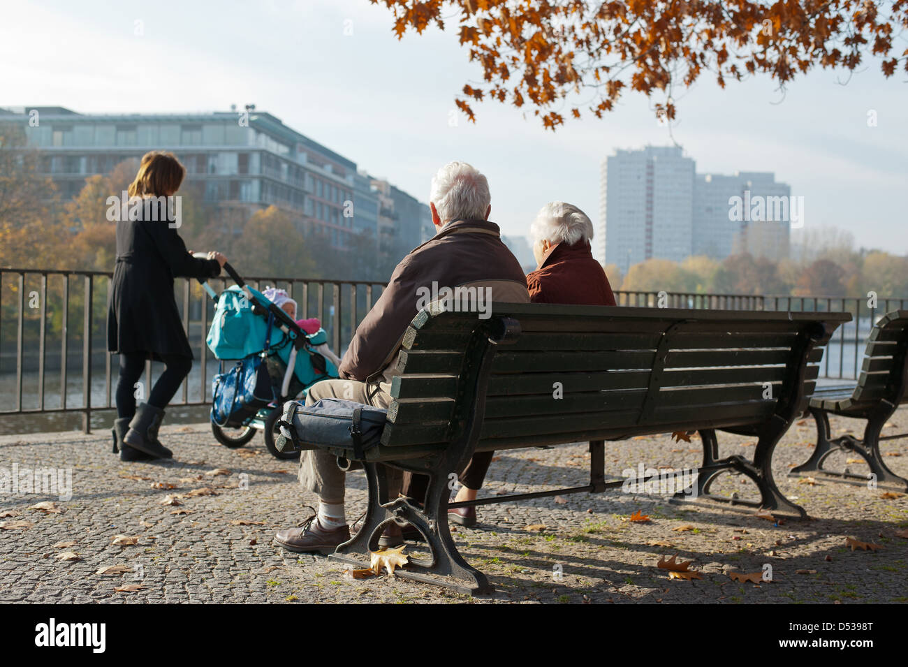 Berlino, Germania, ritirato su una panchina nel parco, madre con bambino trasporto passa Foto Stock