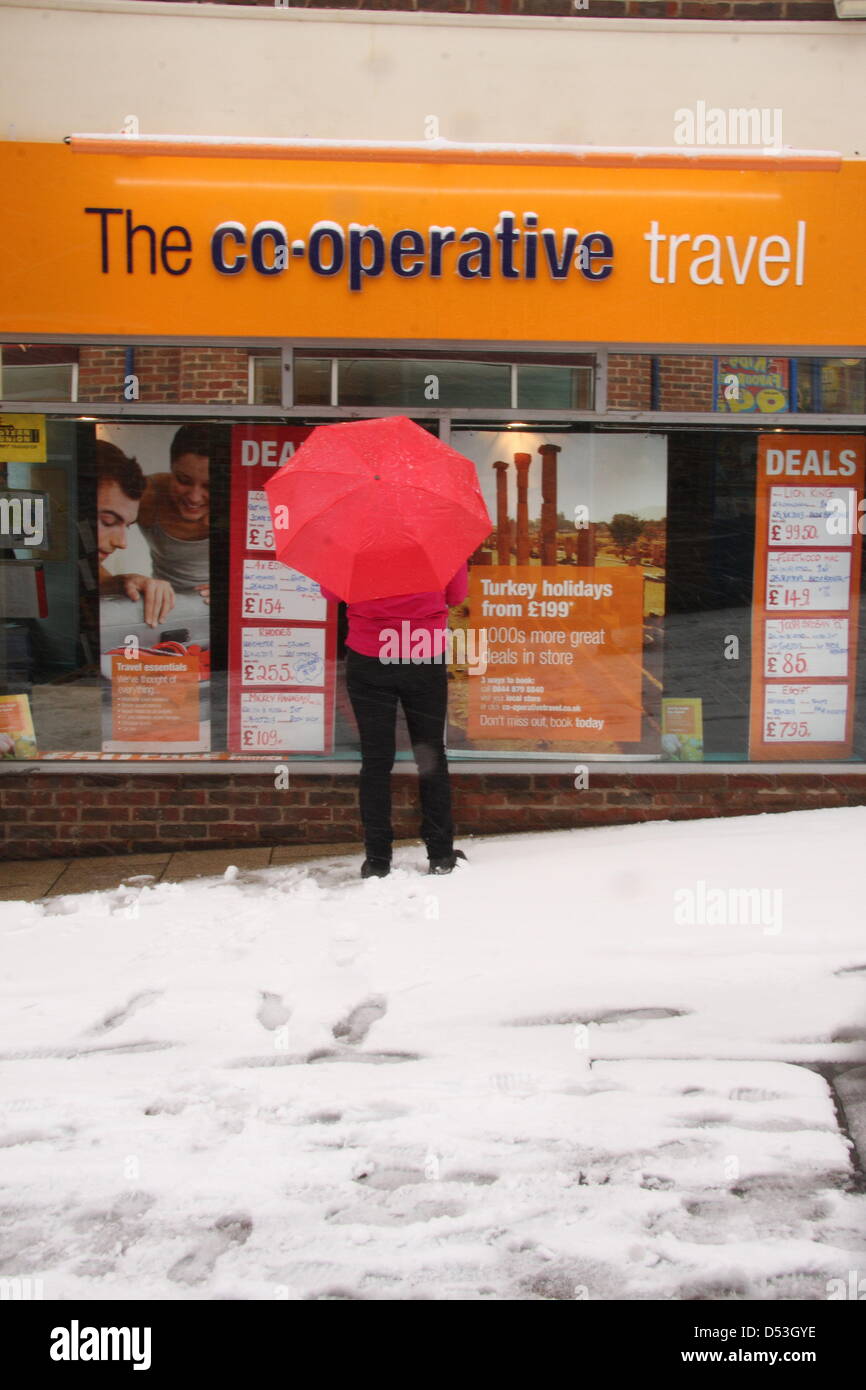 Shopper sogni di climi più soleggiato al travel agent finestra della molla durante la tempesta di neve, Regno Unito, Foto Stock