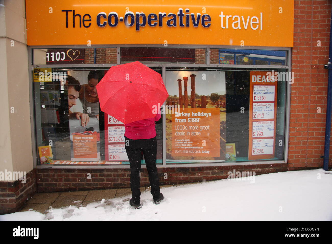 Shopper sogni di climi più soleggiato al travel agent finestra della molla durante la tempesta di neve, Regno Unito, Foto Stock
